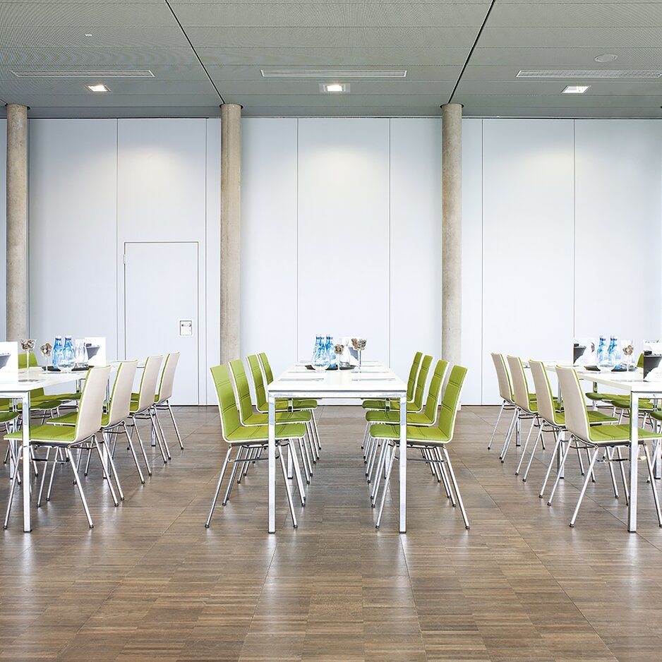 een eetzaal met rechthoekige tafels en stoelen met groene bekleding