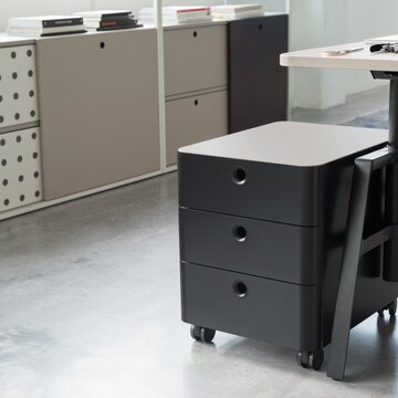 un conteneur à rouleaux noir avec trois tiroirs à côté d’un bureau avec une armoire coulissante à l’arrière-plan