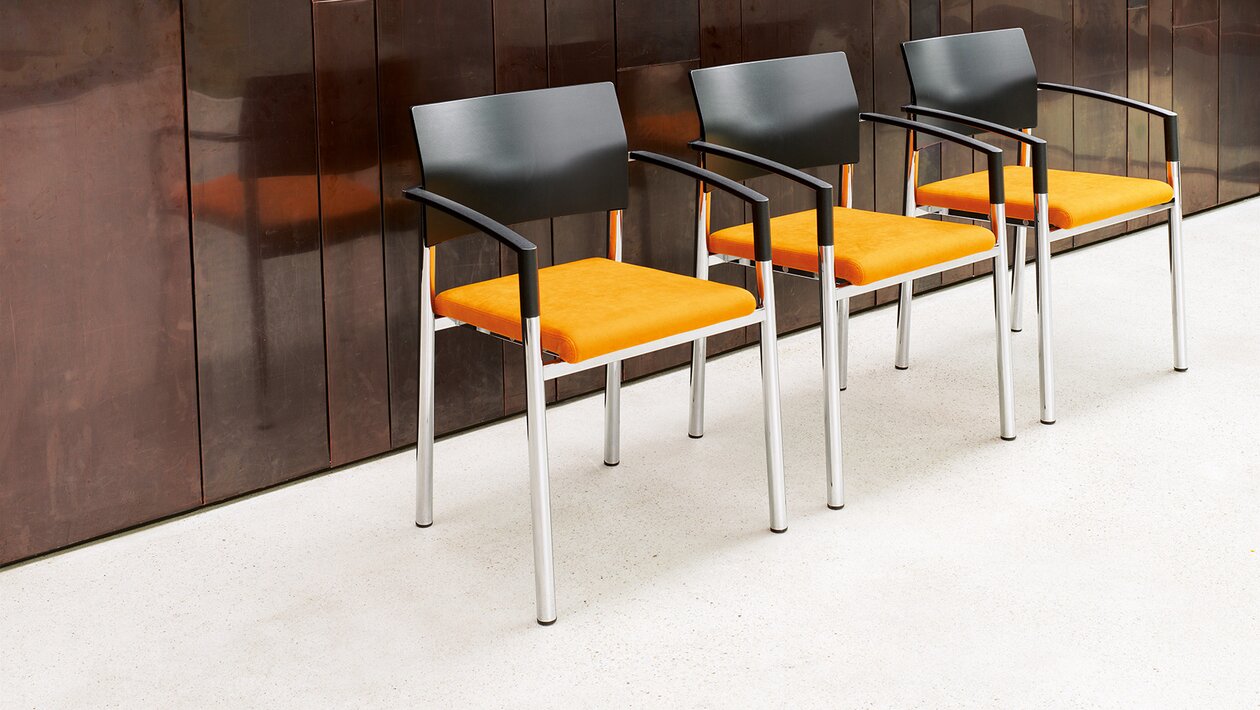 Drei Stühle mit orangem Sitz in einem Raum. 