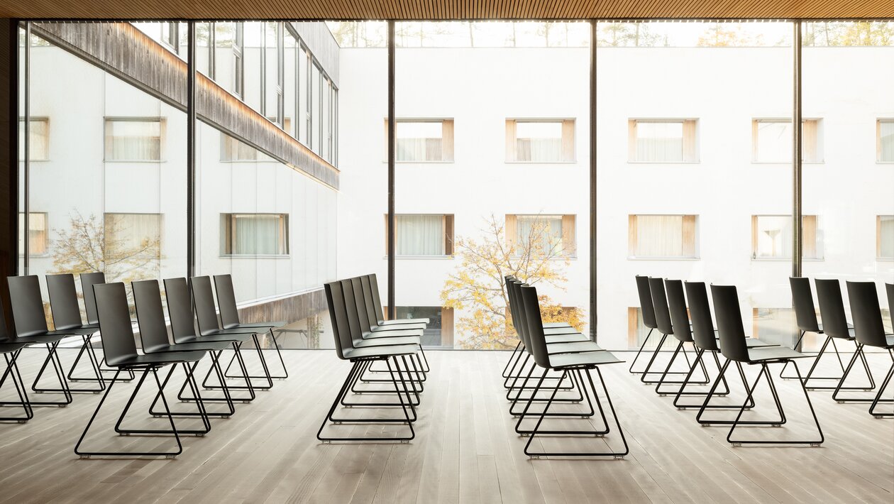 Black rows of chairs in a glazed room with a wooden floor. 