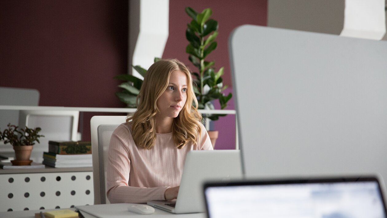 A person sitting on an office desk in front of a notebook.