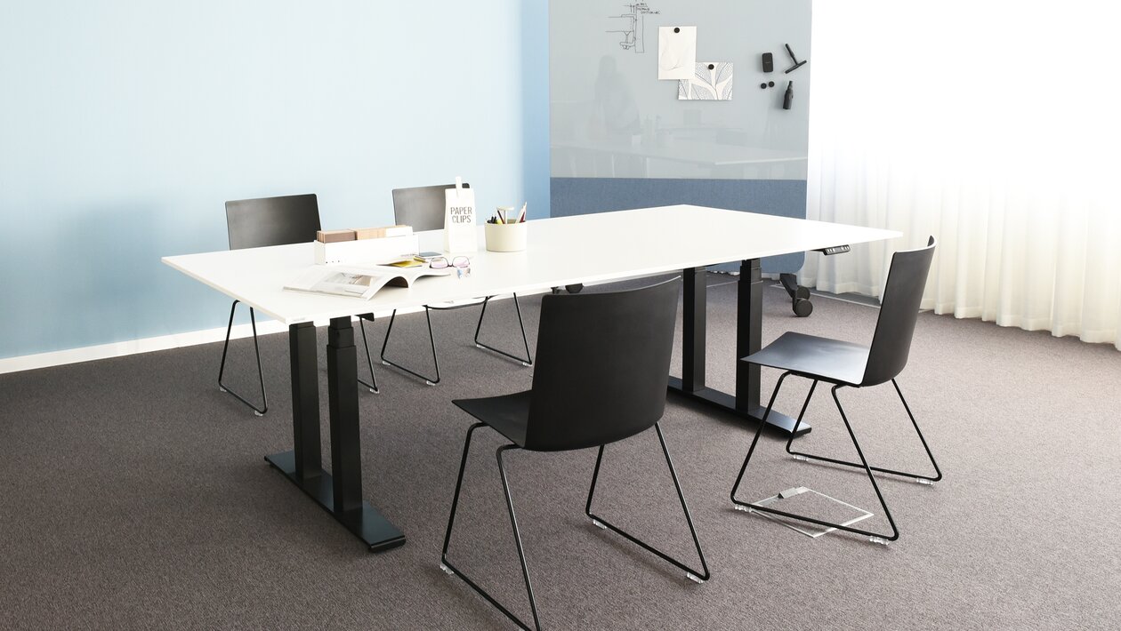 Conference table with four black skid-base chairs in a room with a blue wall.