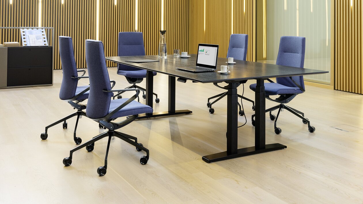 Dark conference table with violet conference chairs in front of a wooden wall.