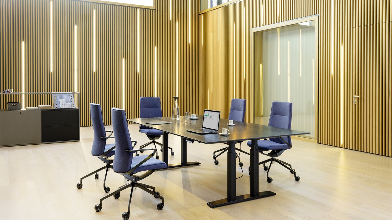 Dunkler Konferenztisch mit violetten Konferenzstühlen vor einer Holzwand. 