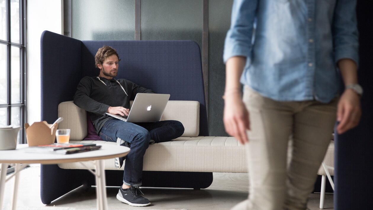 Eine Person arbeitet mit ihrem Laptop auf einem Canapé.