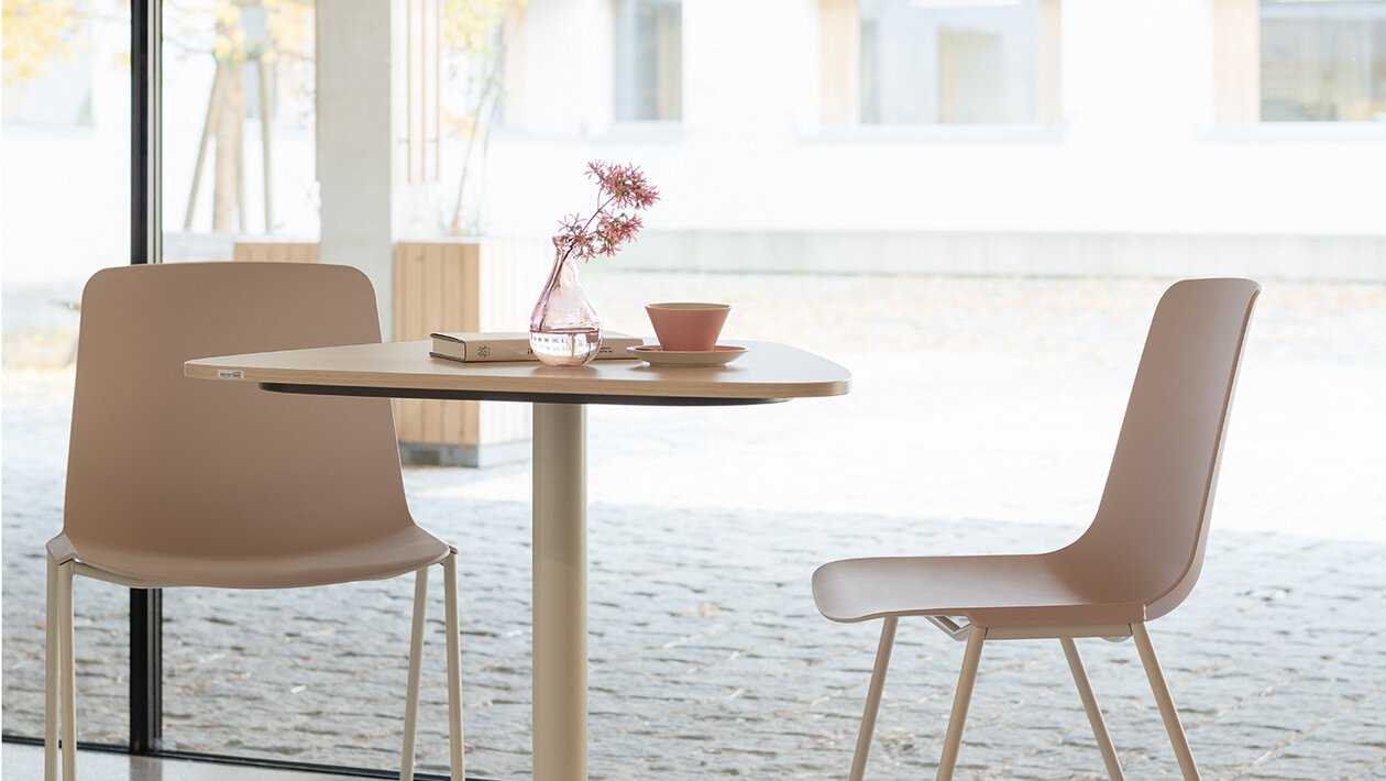 twee grijsroze stoelen en een witte bistrotafel voor een glaswand