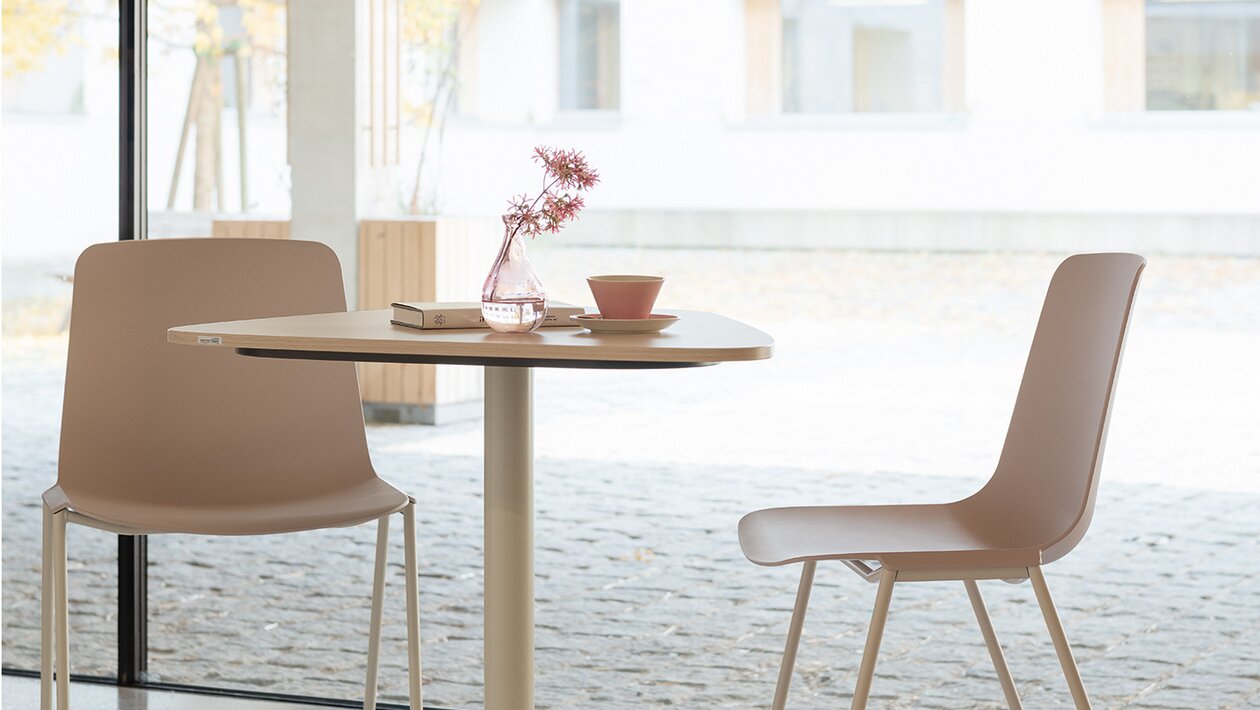 deux chaises gris-rose et une table de bistro blanche devant un mur de verre