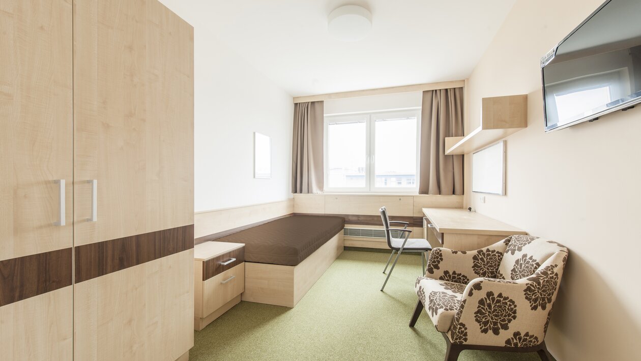 Brown bedroom with bed, cabinet, desk and lounge seating.