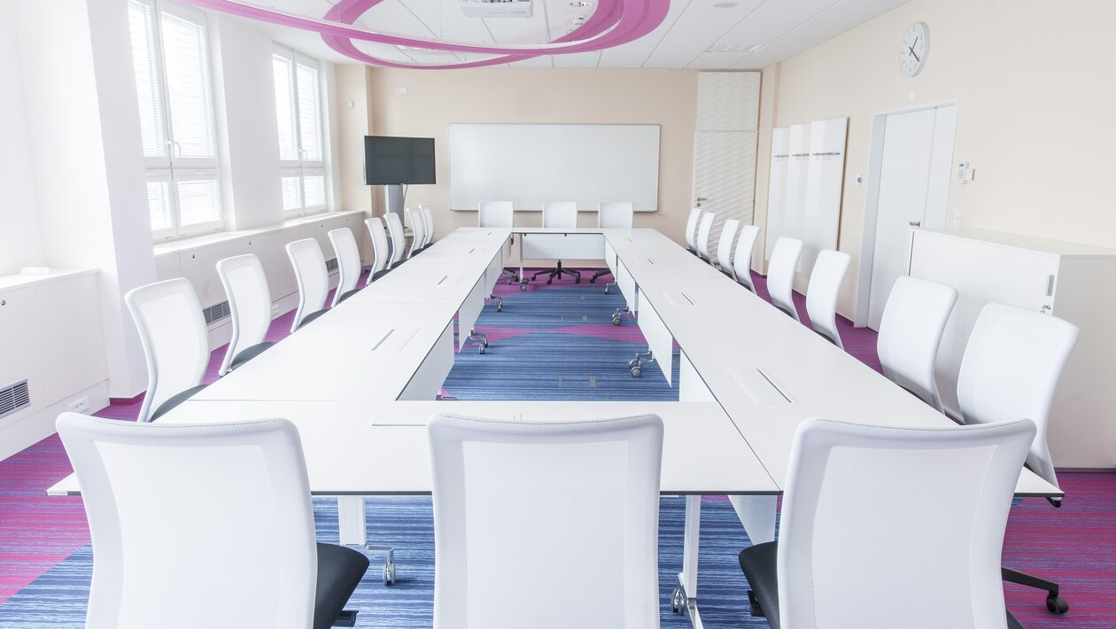 Light meeting room with a white conference table and white conference chairs.