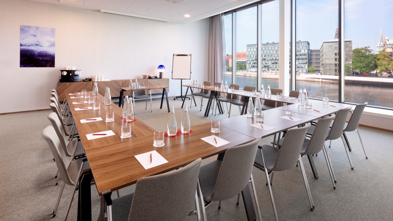 Bright seminar room where the tables have been organised in a U shape. 