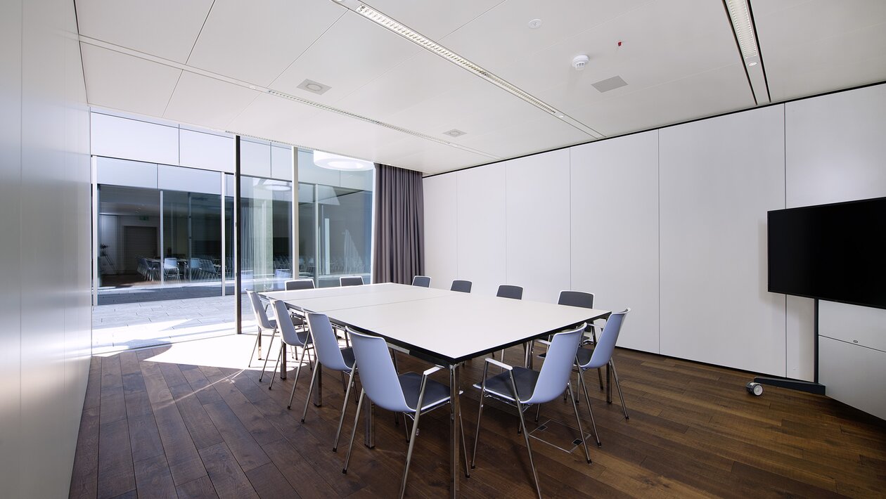Salle de conférence vitrée avec table blanche et chaises bleues.  | © Pichler Fotografen, Urs Pichler