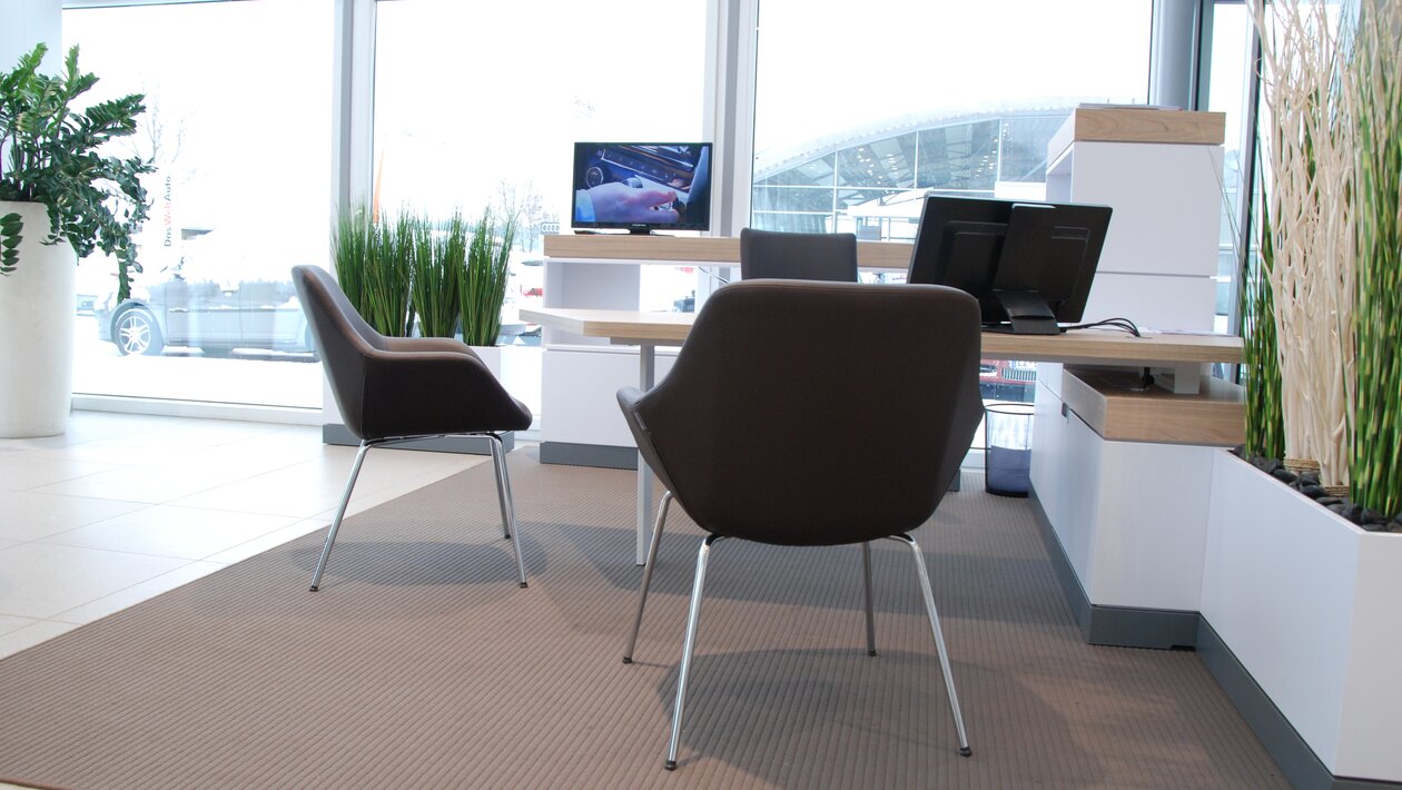 Braune Konferenzstühle vor einem weißen Schreibtisch mit schwarzem Drehstuhl.