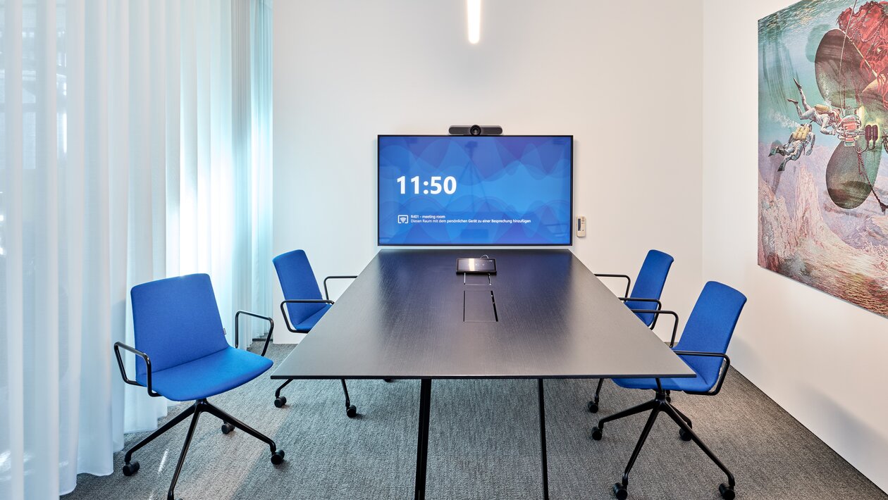 Meeting room with blue conference chairs and a dark table. | © raumpixel.at