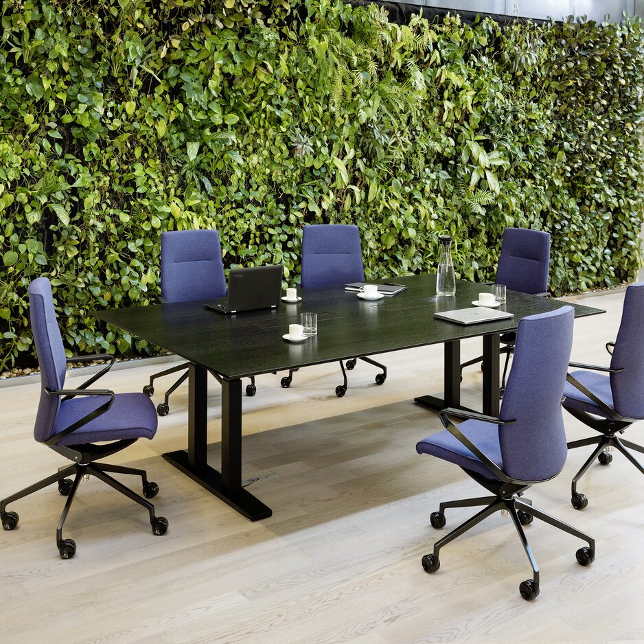 Dark conference table with violet conference chairs in front of a plant wall.