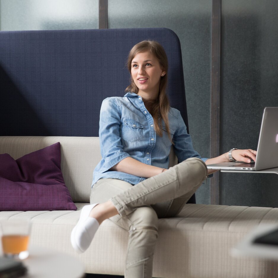 Person sitzt mit einem Laptop auf einem Fauteuil.