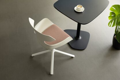 Raum mit einem schwarzen Tisch und einem weißen Schalenstuhl mit Polsterung und 4 Beinen