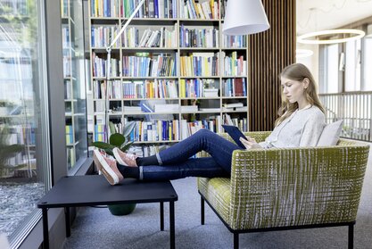 Person sitzt auf einem Polstermöbel und arbeitet an einem Tablet.