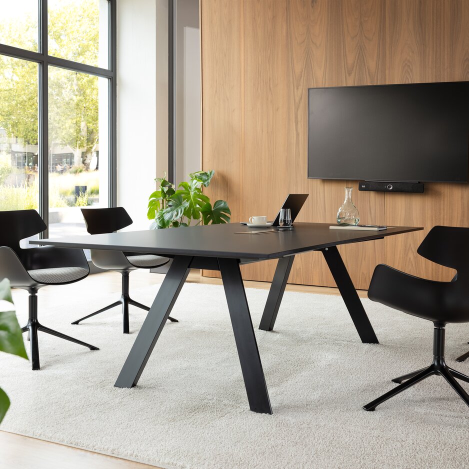 Kamer met een televisie, een grote tafel en zwarte kuipstoelen met grijze bekleding en vier poten