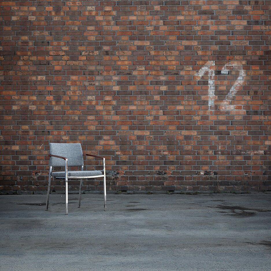 een grijs gestoffeerde stoel met armleuningen voor een bakstenen muur
