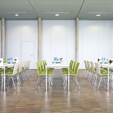 een eetzaal met rechthoekige tafels en stoelen met groene bekleding
