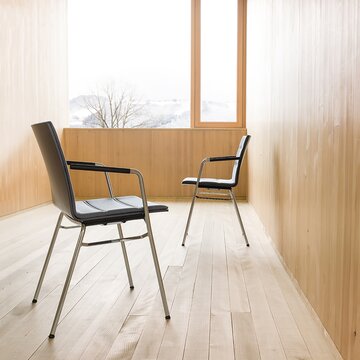 Zwei schwarze Reihenstühle in einem Raum mit Holzwänden und Parkettboden.