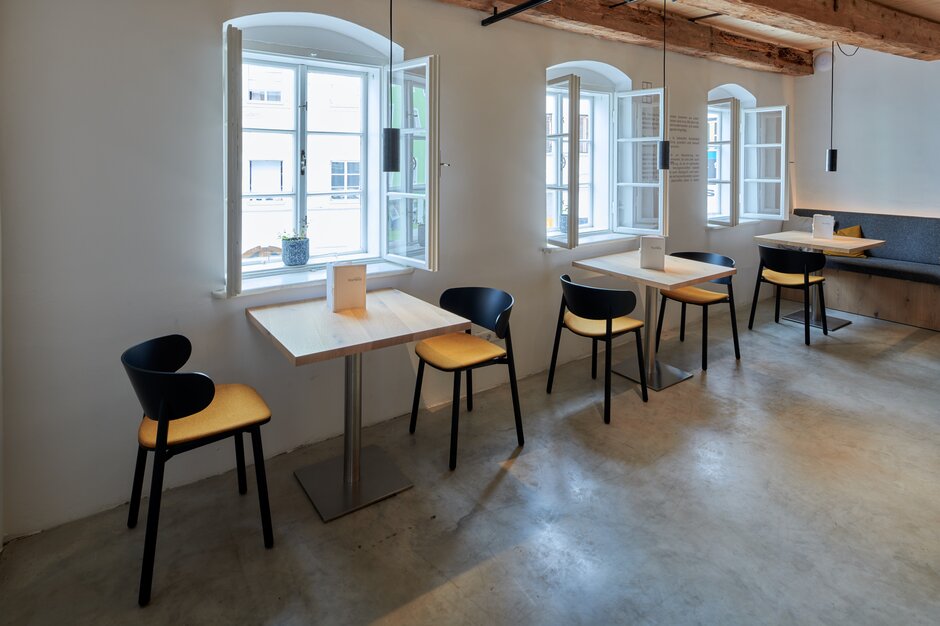 Bistrotables and chairs at a wall with small windows. | © raumpixel.at