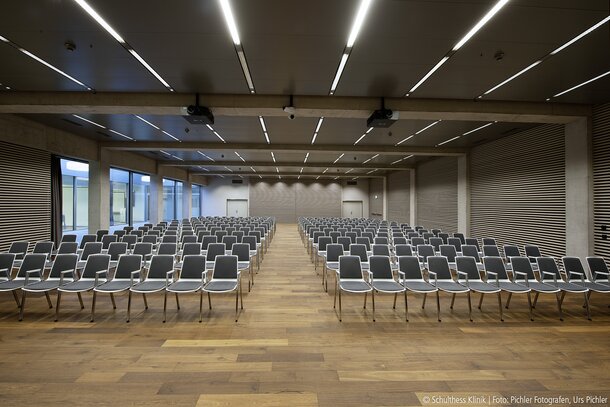 Großer Saal mit schwarz-weißen Reihenstühlen auf einem Holzboden.  | © Pichler Fotografen, Urs Pichler