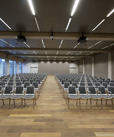 Grande salle avec des chaises alignées en noir et blanc sur un plancher en bois.  | © Pichler Fotografen, Urs Pichler