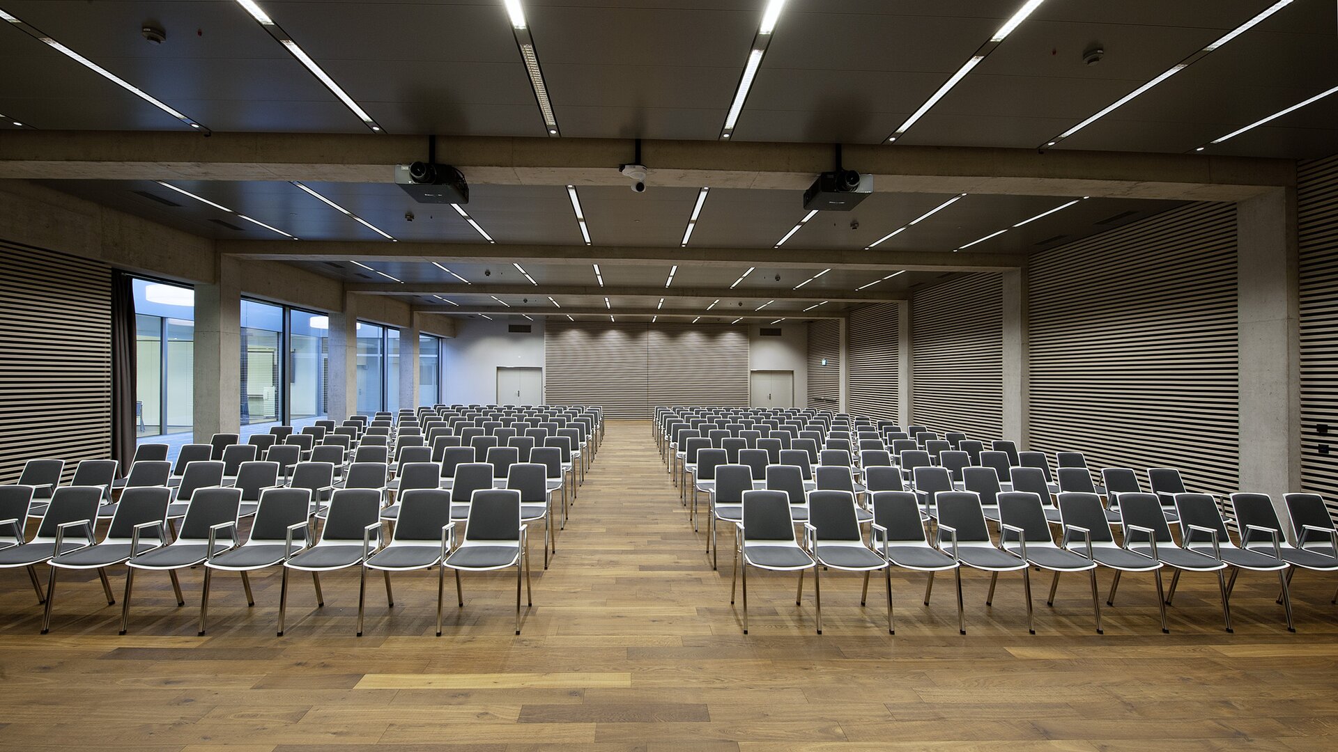 Grande salle avec des chaises alignées en noir et blanc sur un plancher en bois.  | © Pichler Fotografen, Urs Pichler