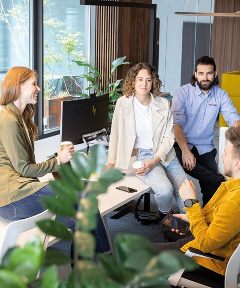 Four people sitting on a workbench talking to each other.