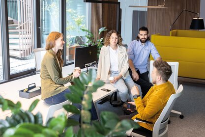 Four people sitting on a workbench talking to each other.