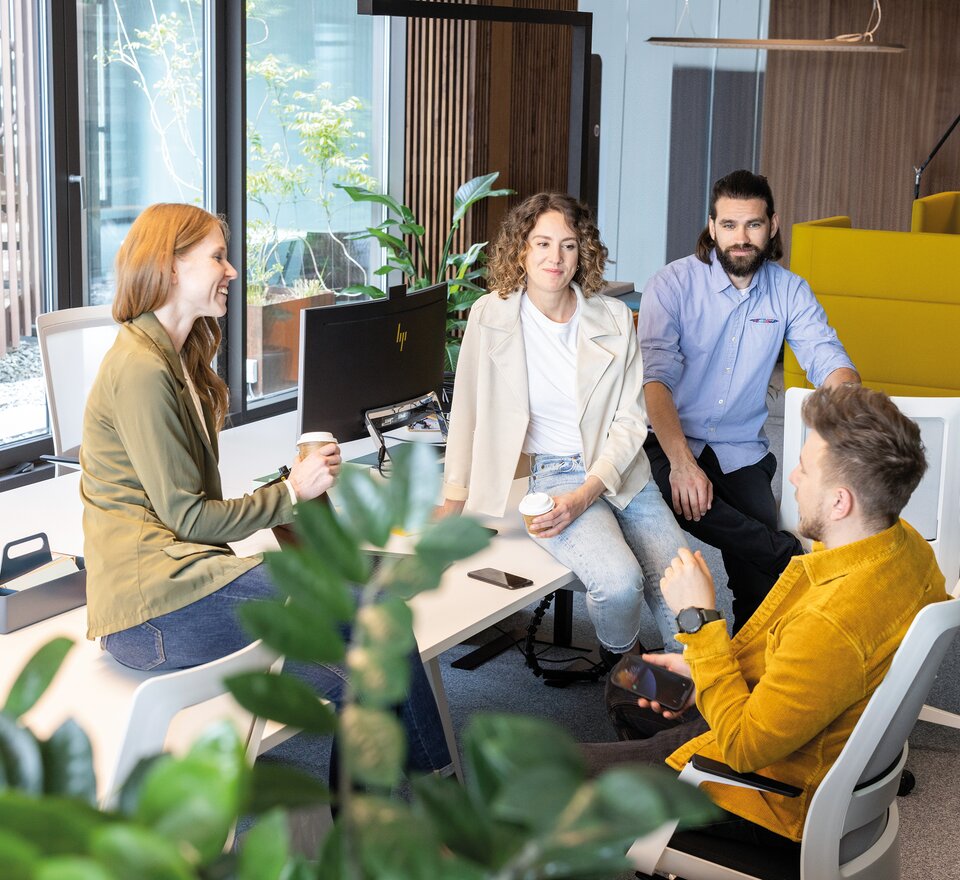 Vier Personen die auf einer Workbench sitzen und sich unterhalten. 