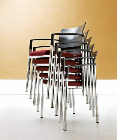 Five stacked chairs with red padded seat and black back.