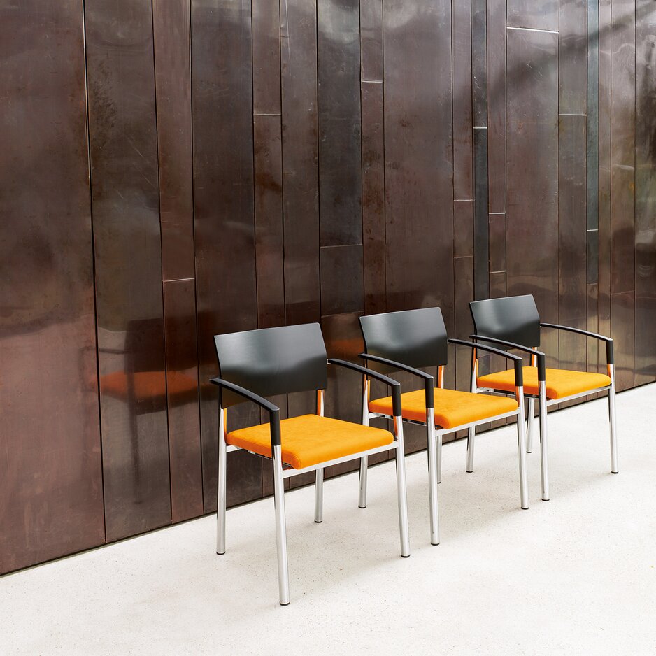 Three chairs with orange seat in a room. 