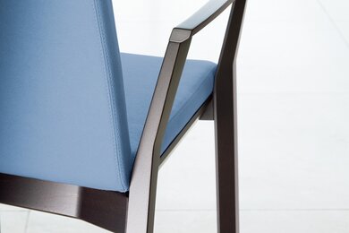 Detailed view of the armrest of a blue padded wooden chair. 