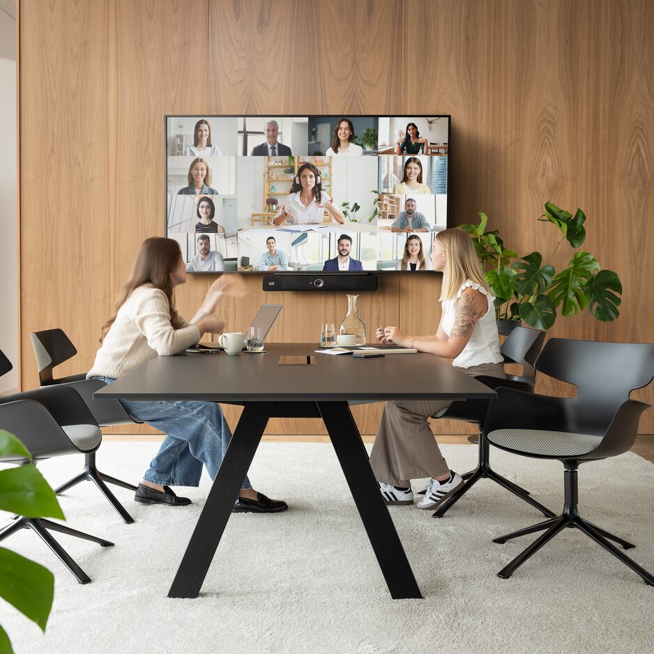 Room with a large television, a black desk, and a black shell chair with grey upholstery and four legs