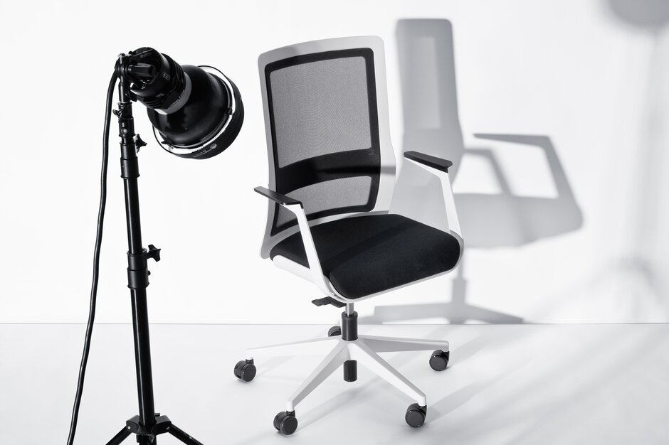White swivel chair with black mesh back and armrest behind a microphone.