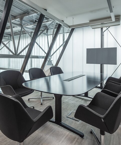 Dunkler Konferenztisch mit Konferenzstühlen in verglastem Büro.