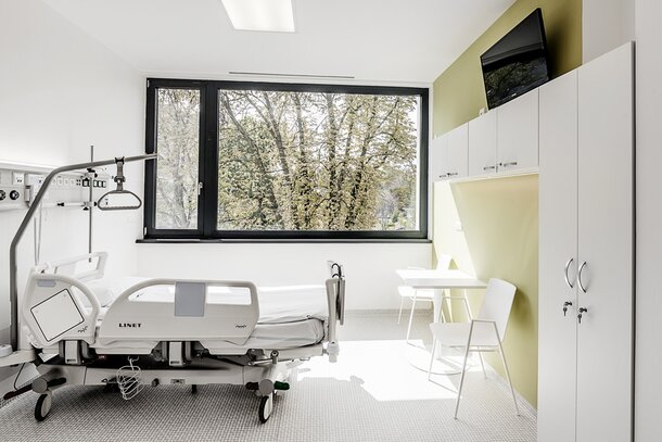 Chambre d’hôpital avec mur vert et mobilier blanc. 