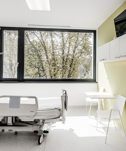 Chambre d’hôpital avec mur vert et mobilier blanc. 