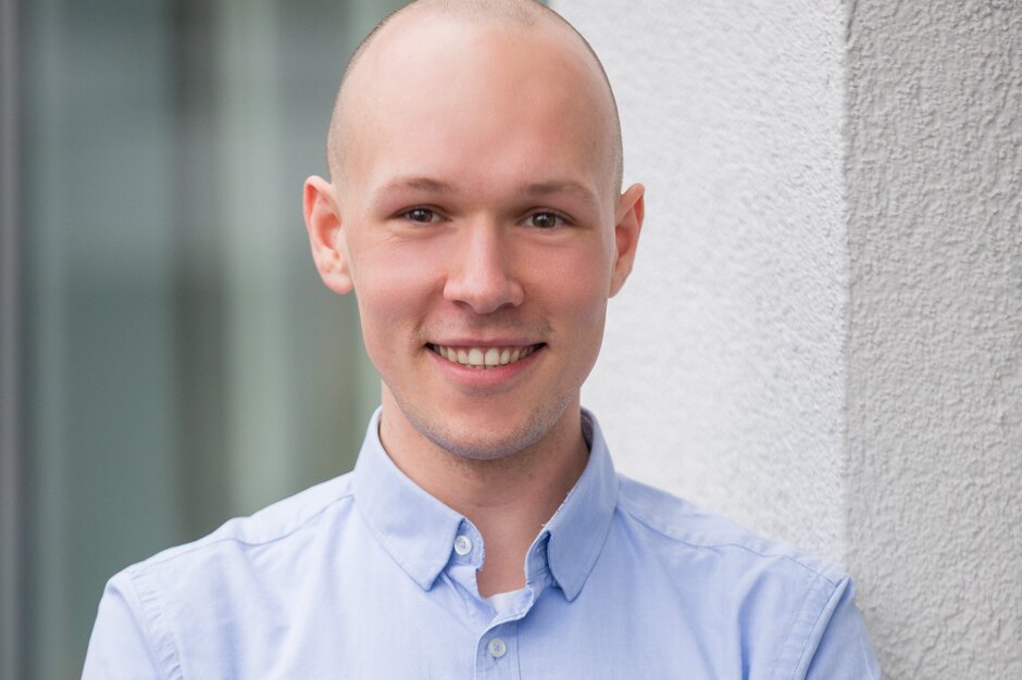 Patrick Berger | © Patrick Berger Mann mit blauem Hemd steht vor einer Wand und hat die Arme verschränkt. | © Patrick Berger
