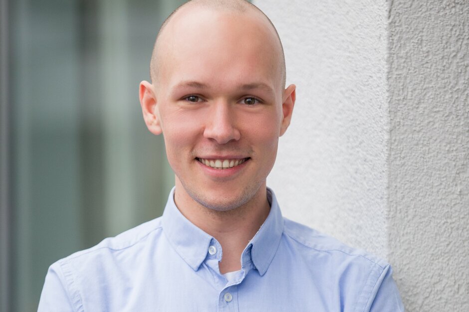 Patrick Berger | © Patrick Berger Mann mit blauem Hemd steht vor einer Wand und hat die Arme verschränkt. | © Patrick Berger
