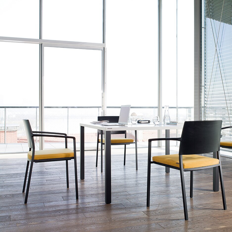 Room with a white table and black chairs with yellow padded seat. 