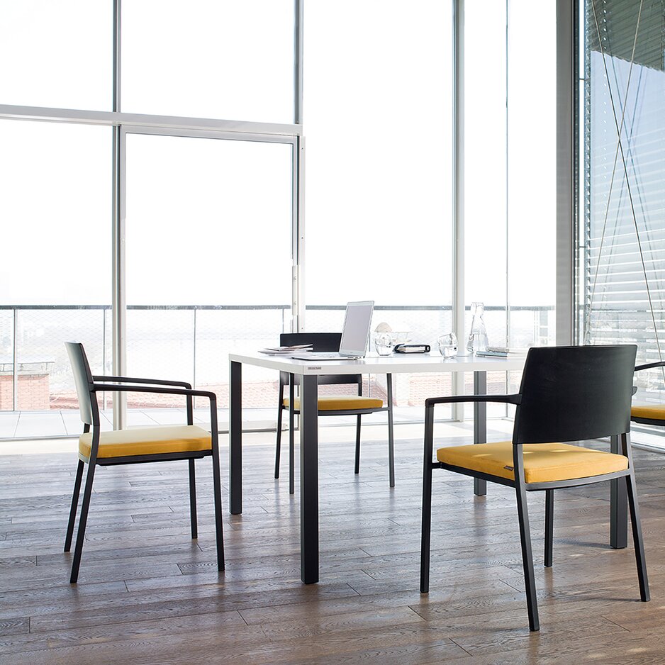 Raum mit einem weißen Tisch und schwarzen Stühlen mit gelb gepolsterten Sitzen. 