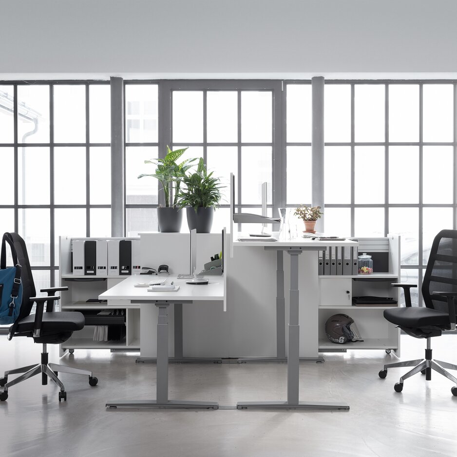 Two gray office desk with two black swivel chairs in a glazed office.