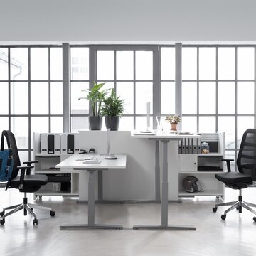 Two gray office desk with two black swivel chairs in a glazed office.
