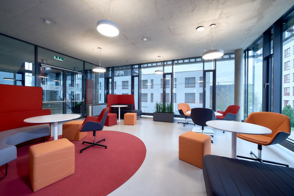 Lernraum mit verschiedenen rot-orangen Möbeln und einer großen Fensterfront. | © raumpixel.at