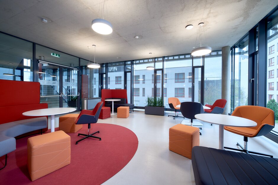 FH IMC | © raumpixel.at Lernraum mit verschiedenen rot-orangen Möbeln und einer großen Fensterfront. | © raumpixel.at