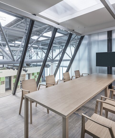 Impact HUB Holzstühle an einem Konferenztisch im verglasten Büro.