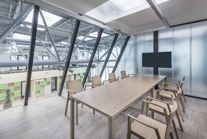Impact HUB Holzstühle an einem Konferenztisch im verglasten Büro.